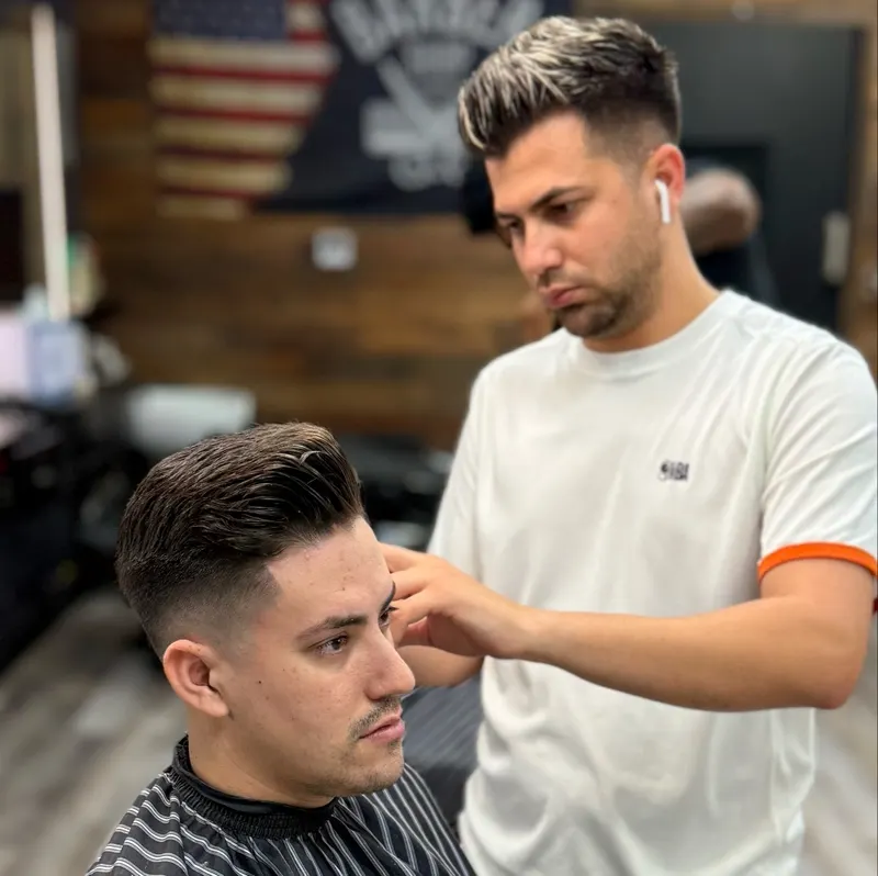 Barber checking a fade on a client, American flag and wood wall behind